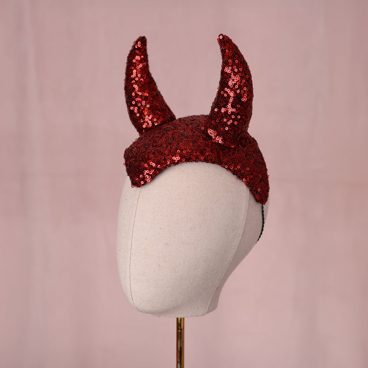 Red sequin devil horns headdress displayed on a white mannequin head against a soft pink background.
