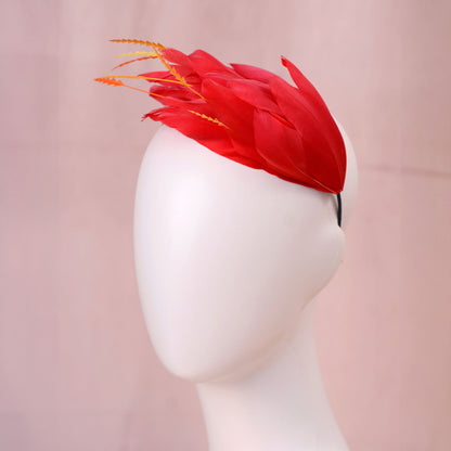 A bright red feather fascinator hat with orange-tipped feathers, displayed on a white mannequin head against a soft pink background.