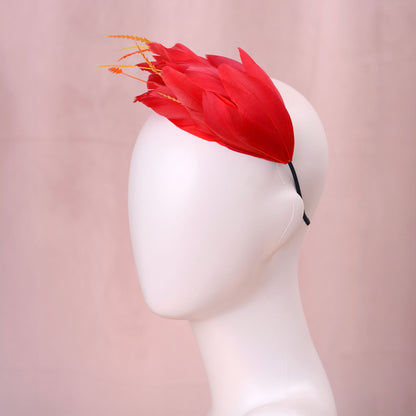 A bright red feather fascinator hat with orange-tipped feathers, displayed on a white mannequin head against a soft pink background.