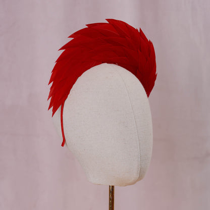 A bright red feather headband styled in a high halo displayed on a white fabric mannequin head against a soft, light pink background front on view three quarter view.