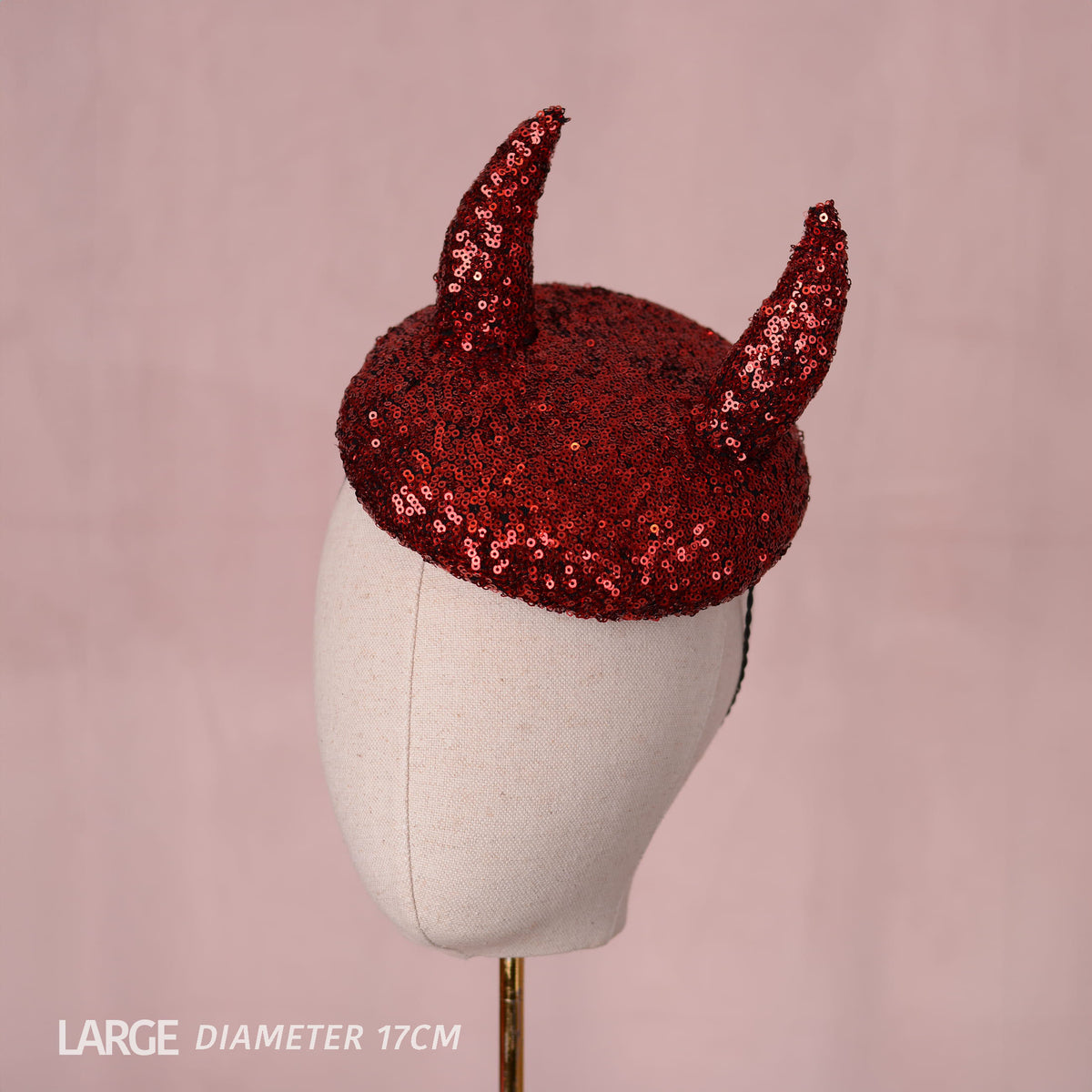 A red sequined horned 3d devil horn hat displayed on a cream-colored mannequin head against a soft pink background. Text in the bottom-left corner reads 'LARGE DIAMETER 17CM'.