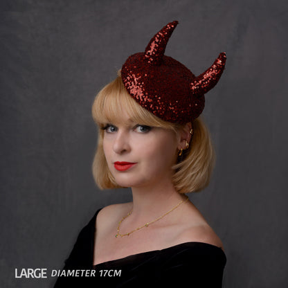 A woman with blonde hair wearing a large, red sequin devil horn fascinator hat against a dark grey studio background. Text overlay at the bottom left reads 'LARGE DIAMETER 17CM'.