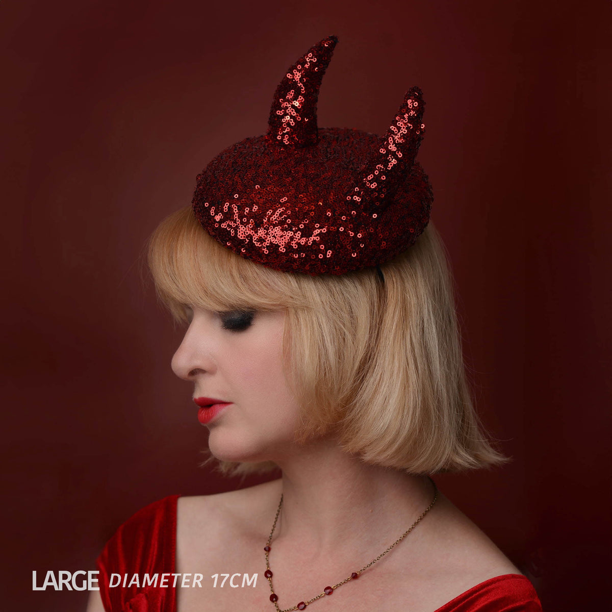 A woman in profile wearing a large red sequined devil horn hat, with text overlay at the bottom left reading 'LARGE DIAMETER 17CM'.
