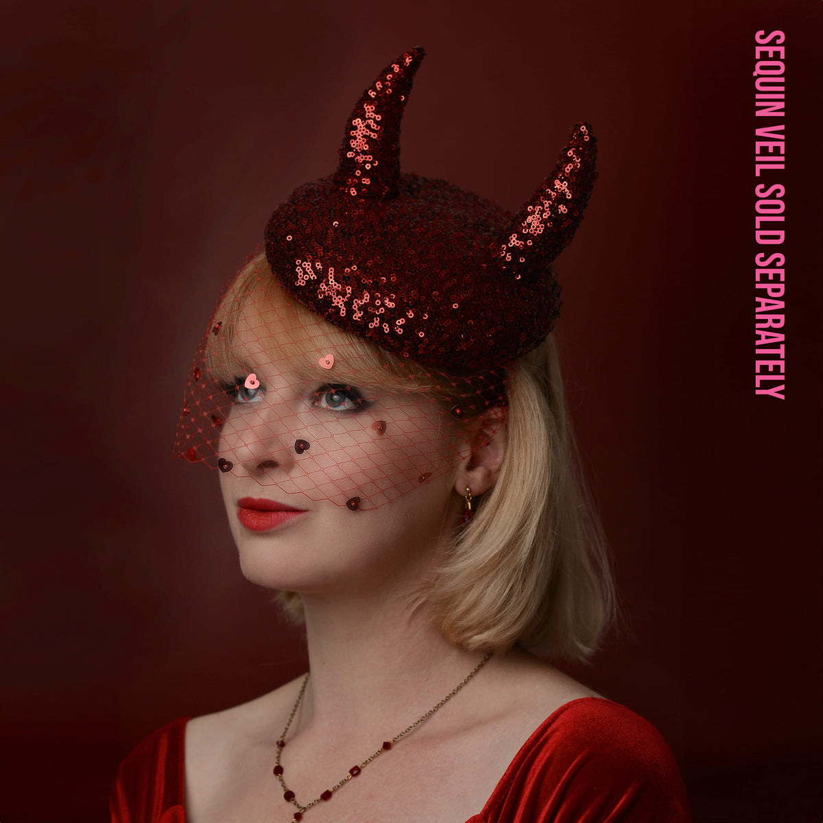 A woman with blonde hair wears a dark red sequin devil horned hat with a matching red netted veil, posed against a dark red background. Pink vertical text on the right reads 'SEQUIN VEIL SOLD SEPARATELY'.