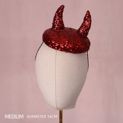 A red sequin devil horn button fascinator displayed on a cream fabric mannequin head against a soft pink background, with text in the lower-left corner reading 'MEDIUM DIAMETER 14CM'.