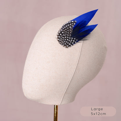 Blue feather hair clip with black and white polka dot design on a mannequin head against a pink background