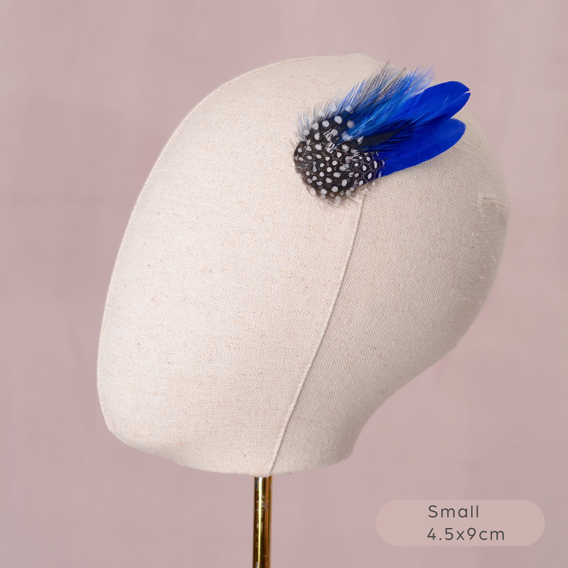 Blue feather hair clip with black and white polka dot design on a mannequin head against a pink background