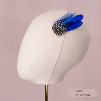 Blue feather hair clip with black and white polka dot design on a mannequin head against a pink background