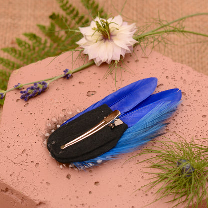 Blue feather hair clip on a pink stone surface with greenery