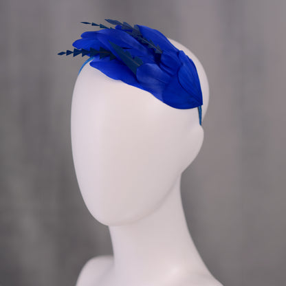 Royal blue feather formal event headpiece on a mannequin head against a grey background