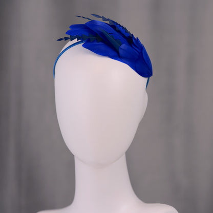 Royal blue feather formal event headpiece on a mannequin head against a grey background