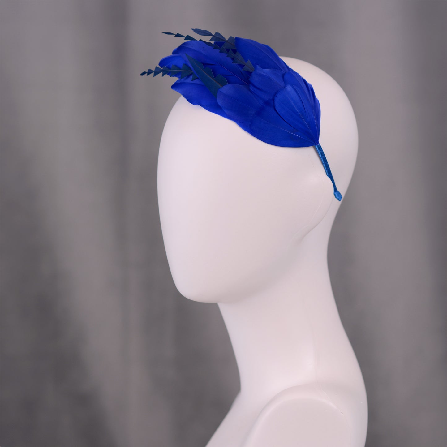 Royal blue feather wedding headband on a mannequin head against a grey background