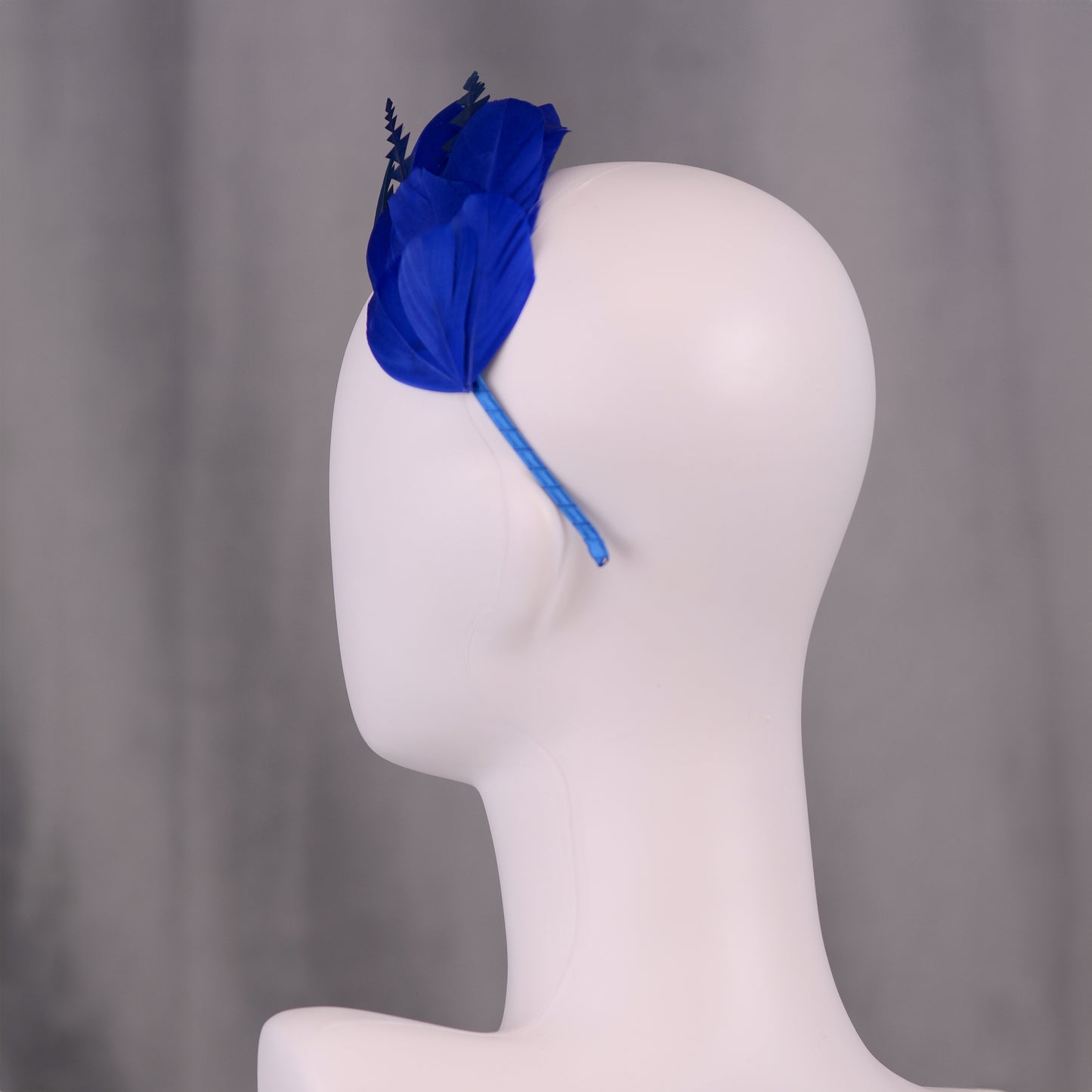 Blue headband with feathers on a mannequin head against a grey background