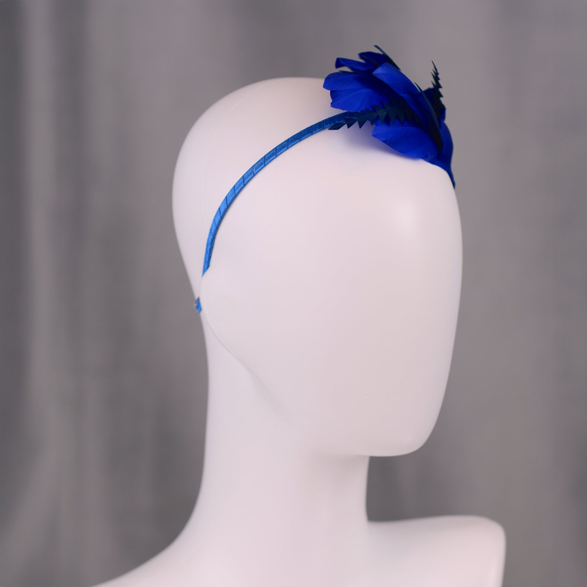 Blue headband with feathers on a mannequin head against a grey background