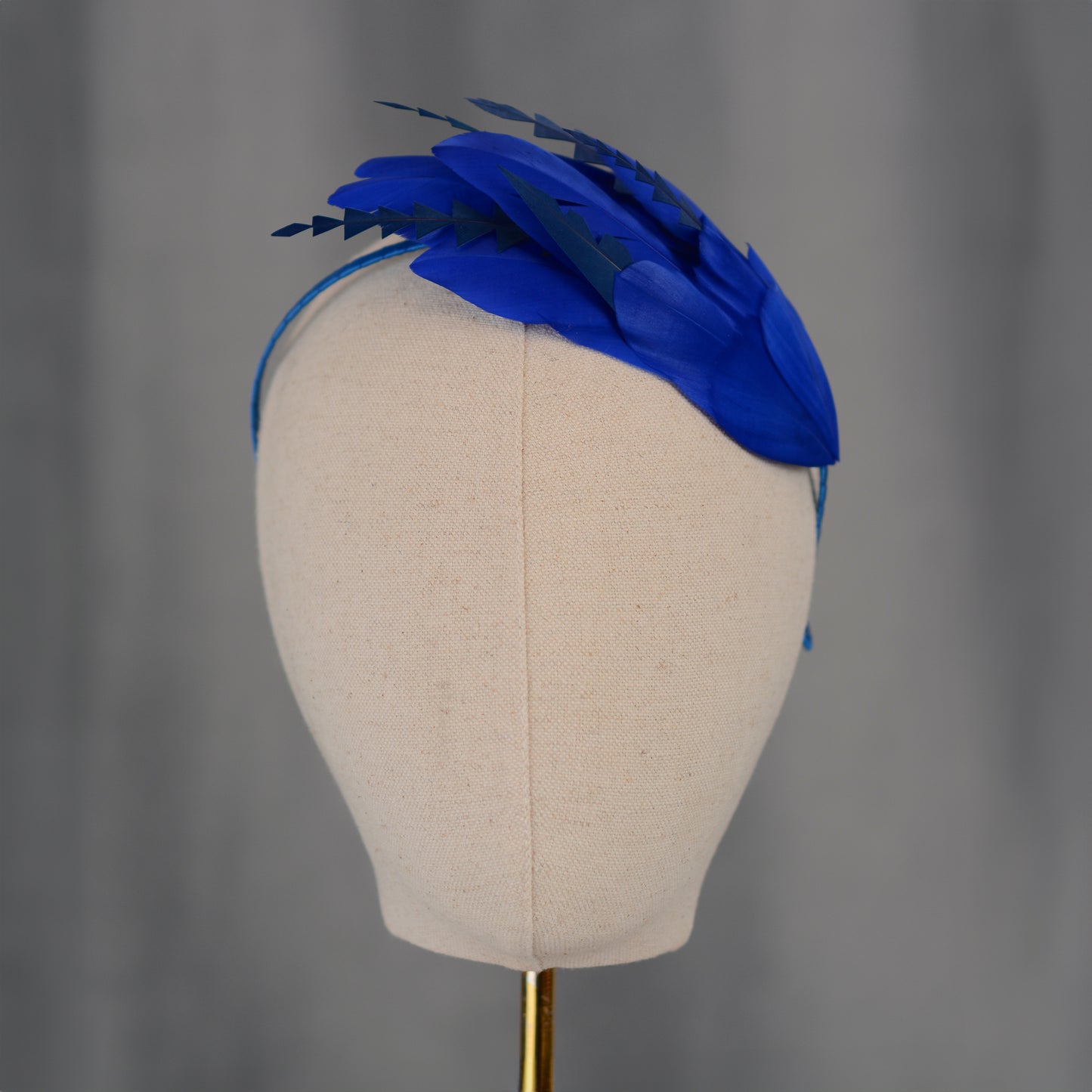 Blue feathered headband on a mannequin head against a grey background