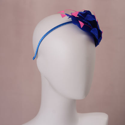 A royal blue headband with side perching floating feather design  with hot pink accent, displayed on a white mannequin head against a soft pink background.