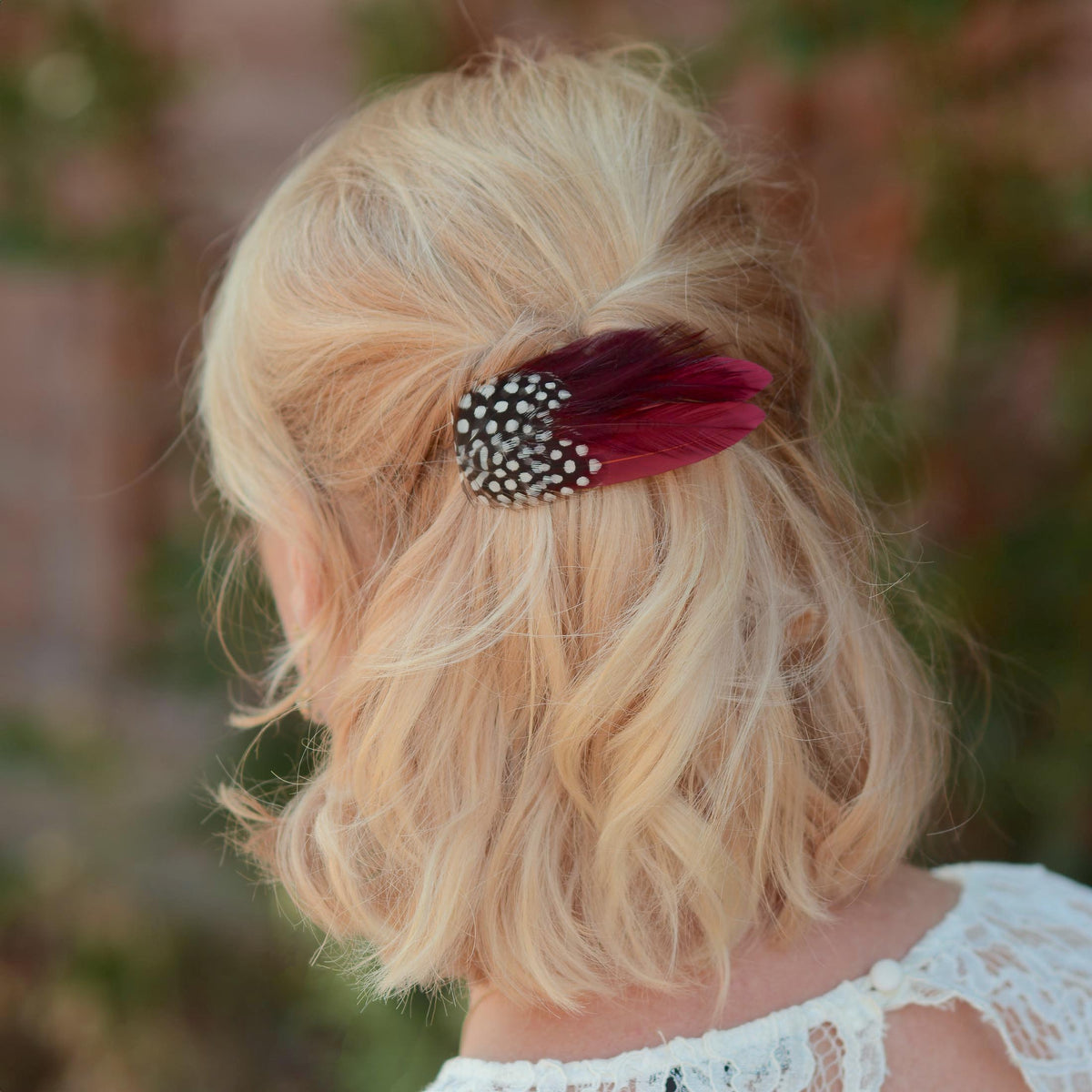 Woman with a blonde bob in a half up do adorned with a small feather hair accessory clip in burgundy and polka dot feathers. Perfect for accessorising a burgundy outfit or burgundy themed wedding.