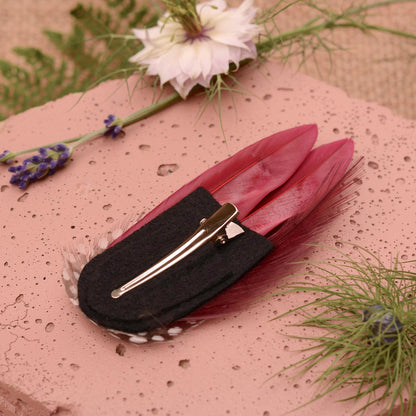 Burgundy feather hair clip on a black felt base with a silver alligator style clip.
