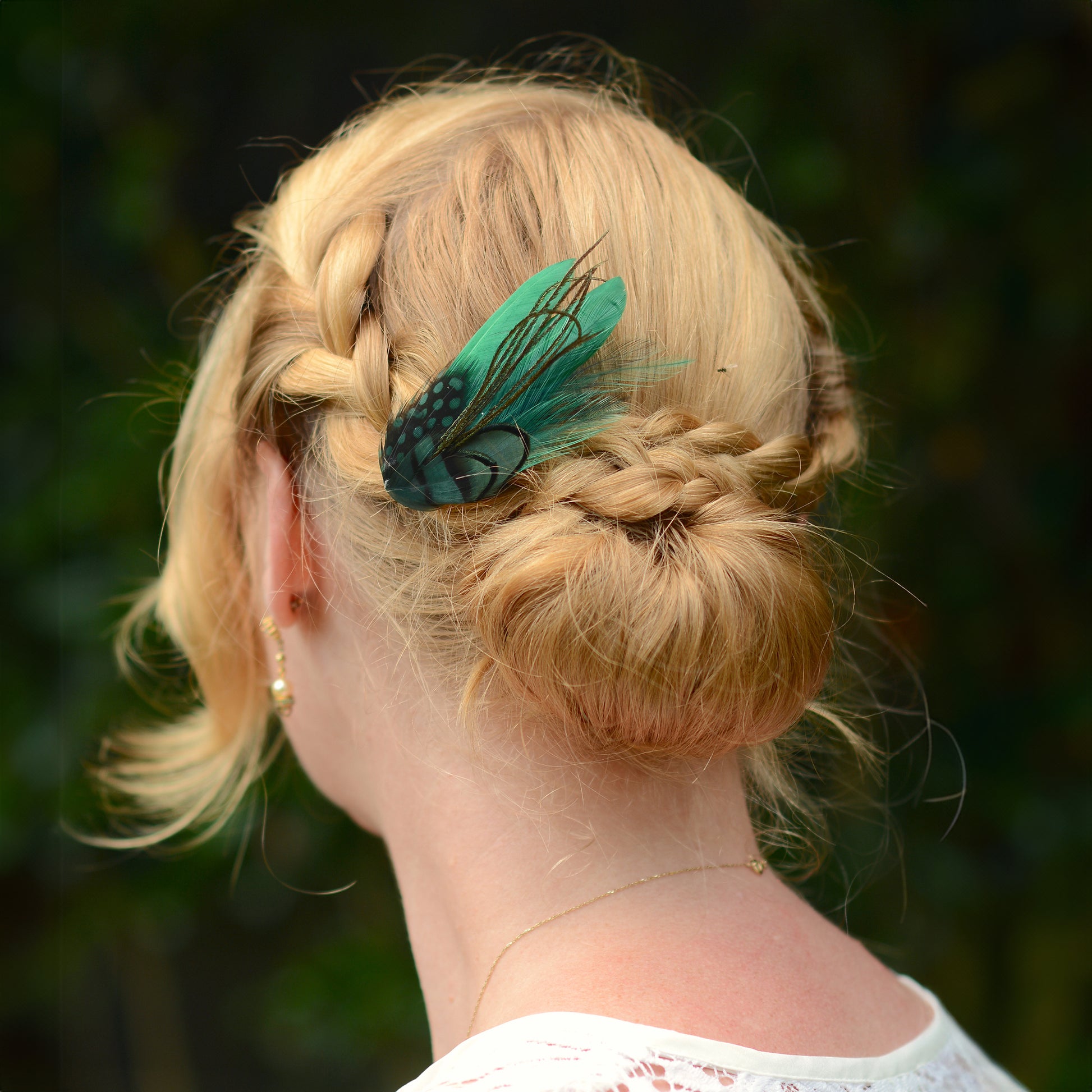 Person with braided hair and a green feather accessory, blurred green background