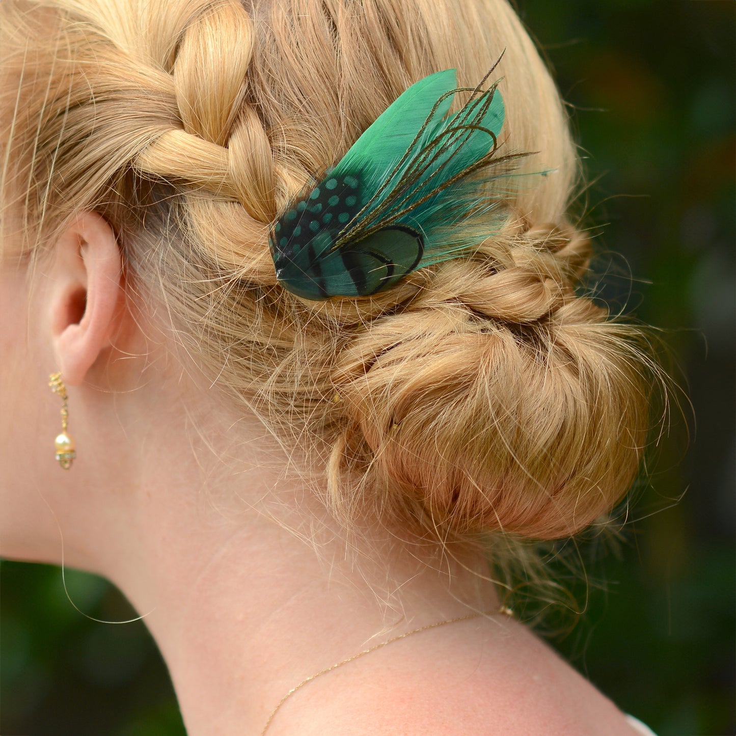 Close-up of a braided hairstyle with a green feather hair accessory against a blurred natural background