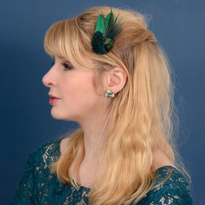 Woman with blonde hair and a green feather hair clip against a blue background