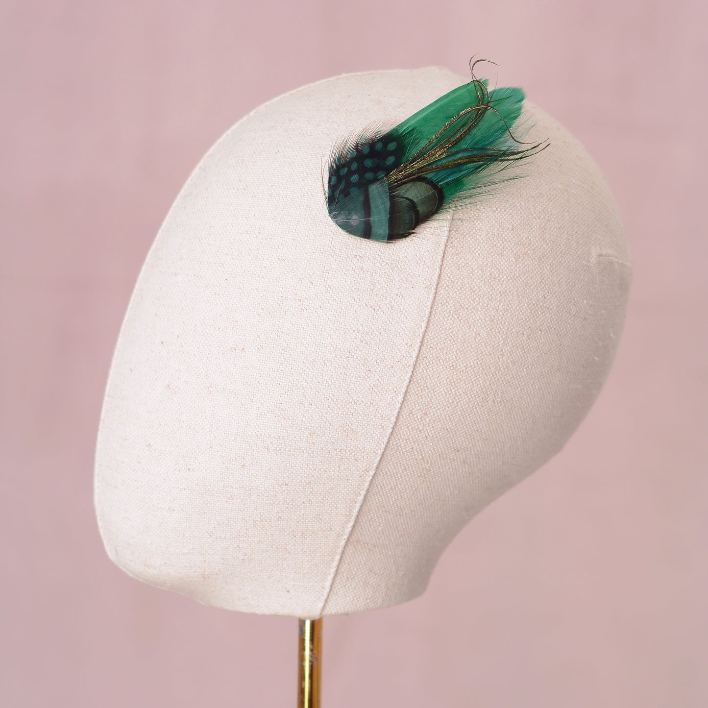 small green feather accessory on a mannequin head against a pink background