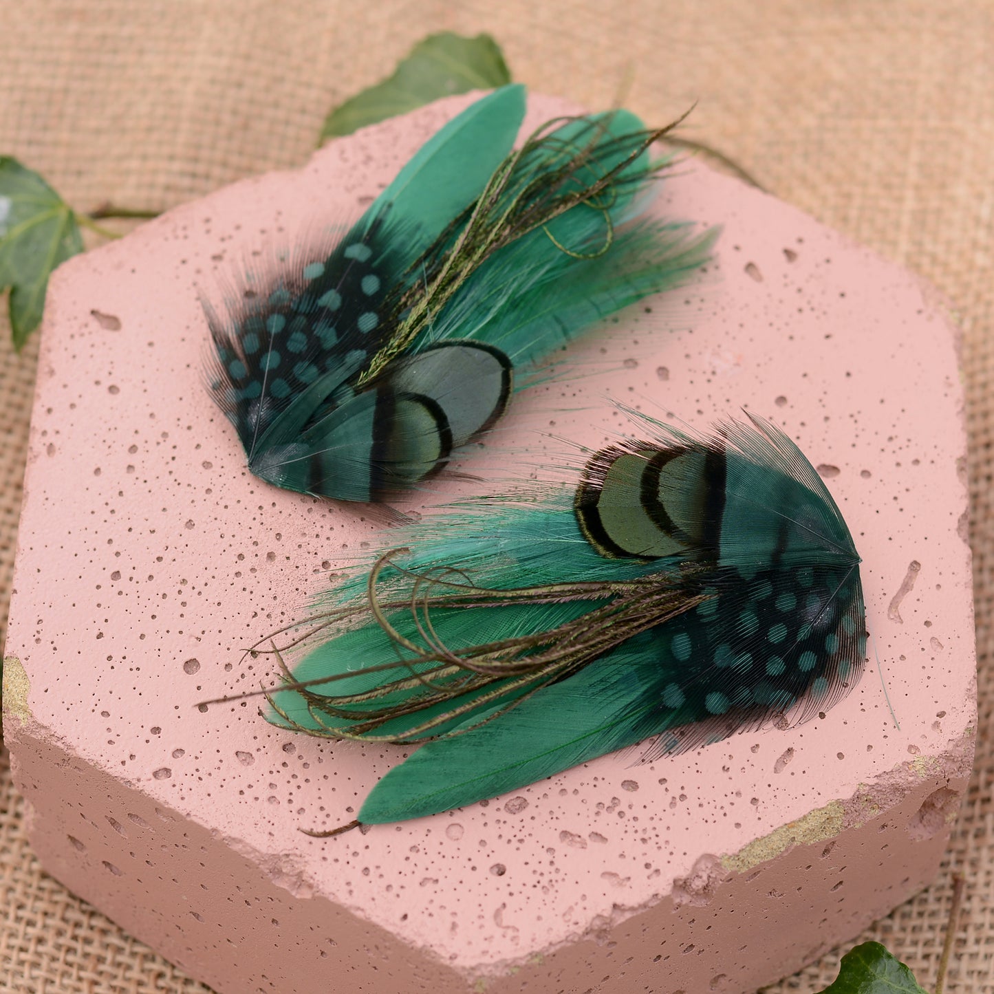 small green feather hair clips on a pink textured stone and beige background