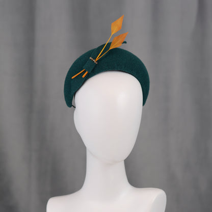 Teal green headband  fascinator with gold yellow feathers and bow on a mannequin with a grey background