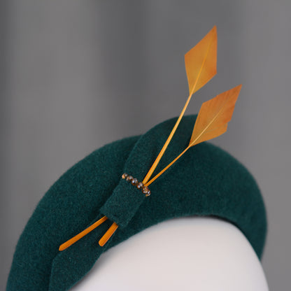 Teal green headband  fascinator with gold yellow feathers and bow on a mannequin with a grey background