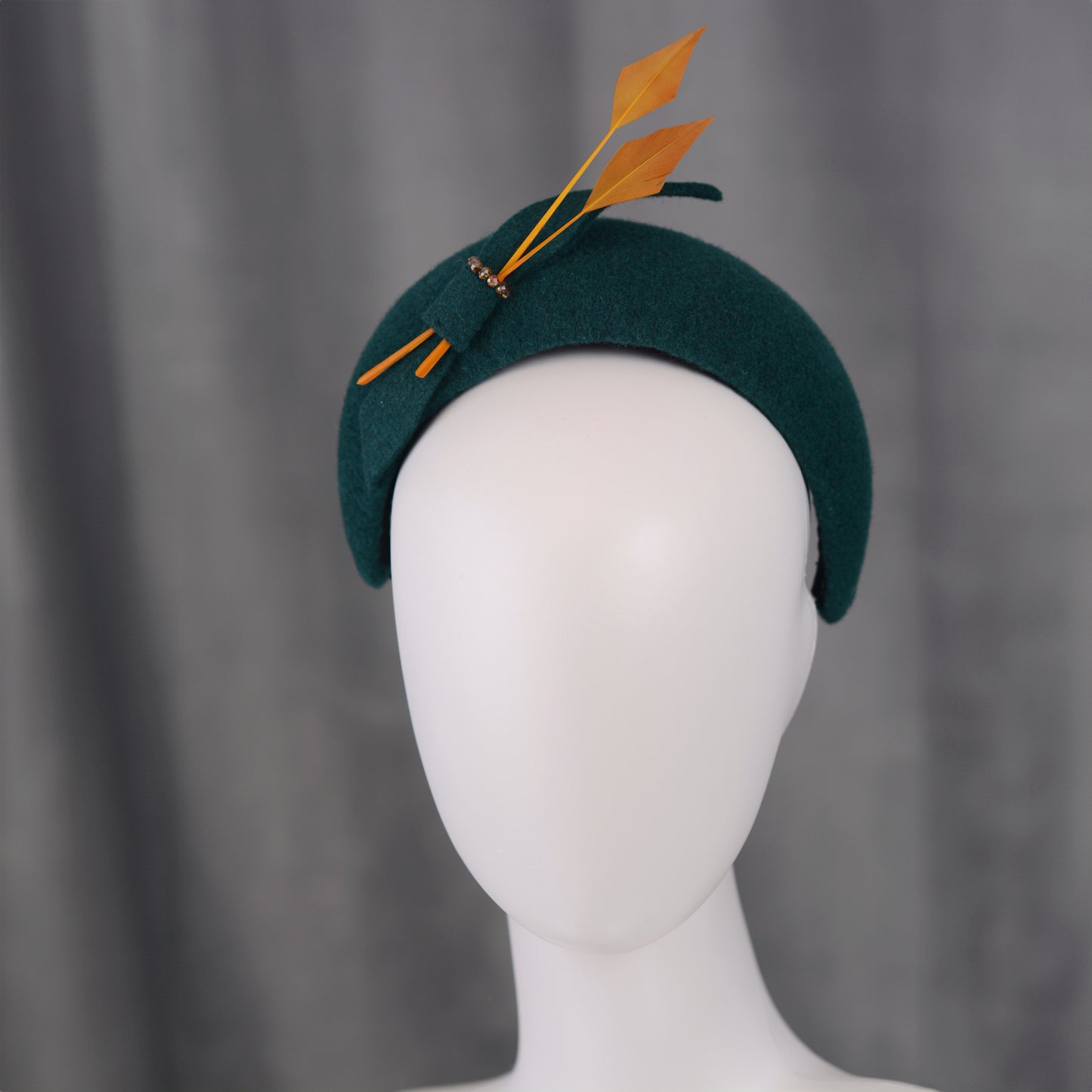 Teal green headband  fascinator with gold yellow feathers and bow on a mannequin with a grey background