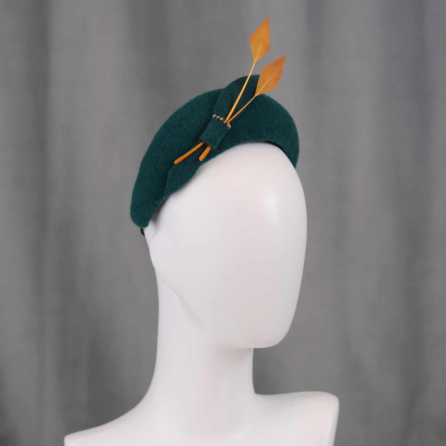 Teal green headband  fascinator with gold yellow feathers and bow on a manequin with a grey background