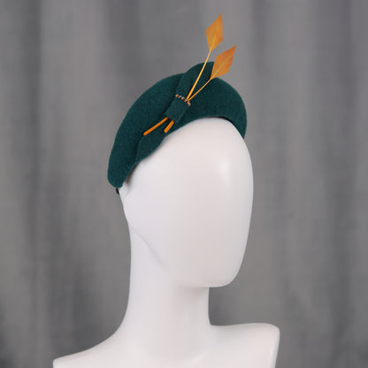 Teal green headband  fascinator with gold yellow feathers and bow on a manequin with a grey background
