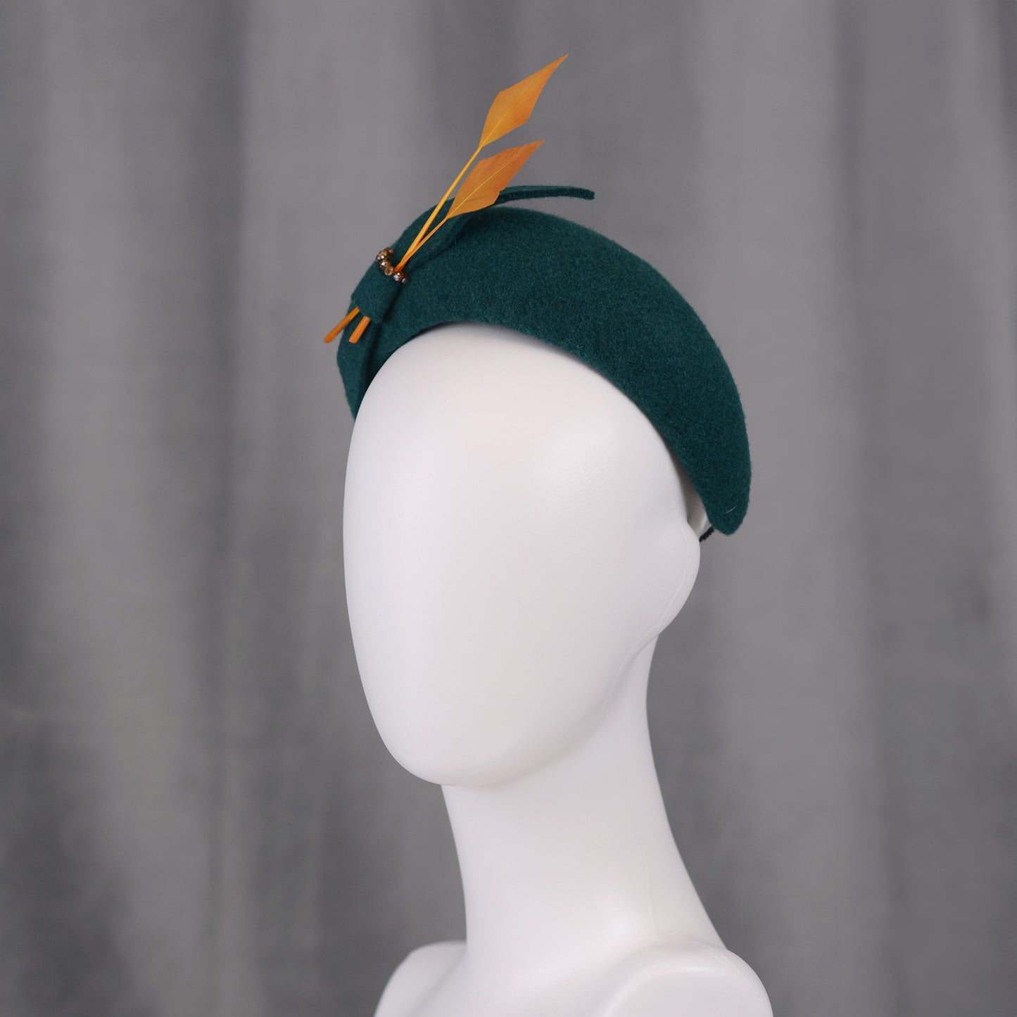 Teal green headband  fascinator with gold yellow feathers and bow on a gray background