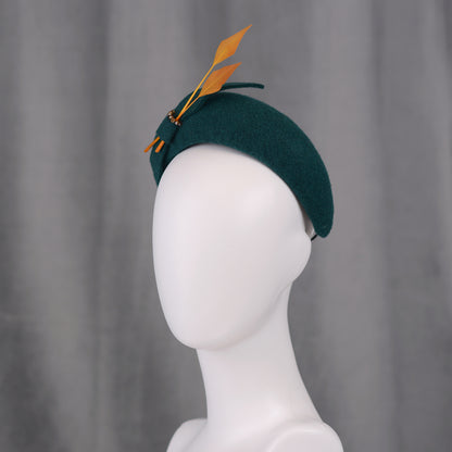 Teal green headband  fascinator with gold yellow feathers and bow on a gray background