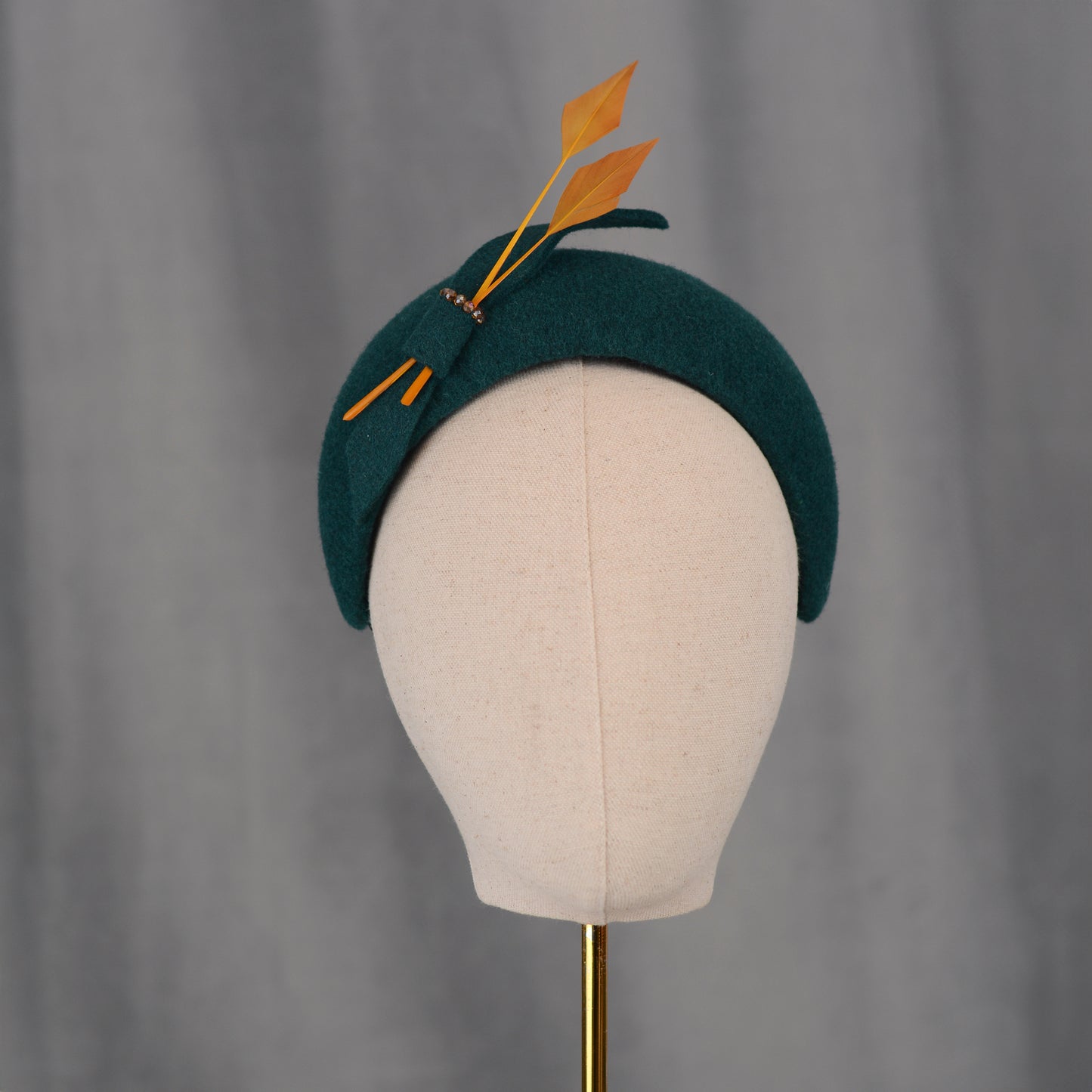 Teal green headband  wedding fascinator with gold yellow feathers and bow on a gray background