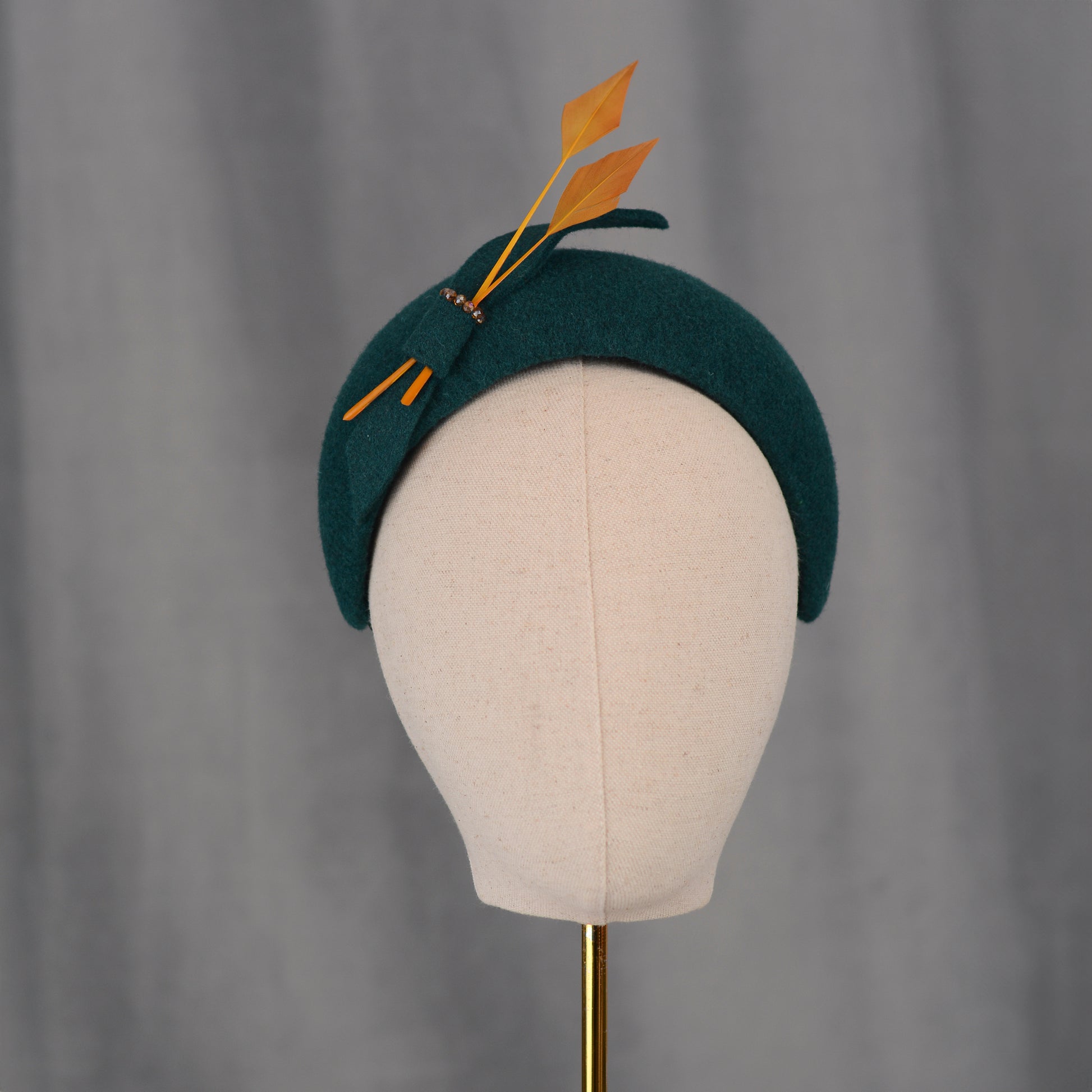 Teal green headband  wedding fascinator with gold yellow feathers and bow on a gray background