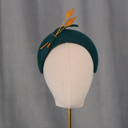 Teal green headband  wedding fascinator with gold yellow feathers and bow on a gray background