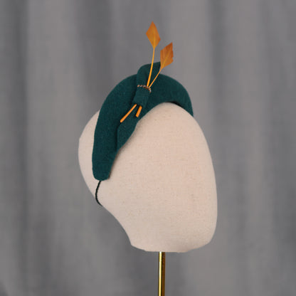 Teal green headband  fascinator with gold yellow feathers and bow on a gray background