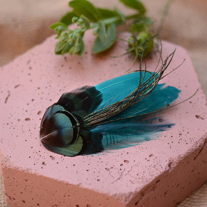 teal feather hair clip with iridescent green feathers on a pink stone background with flowers