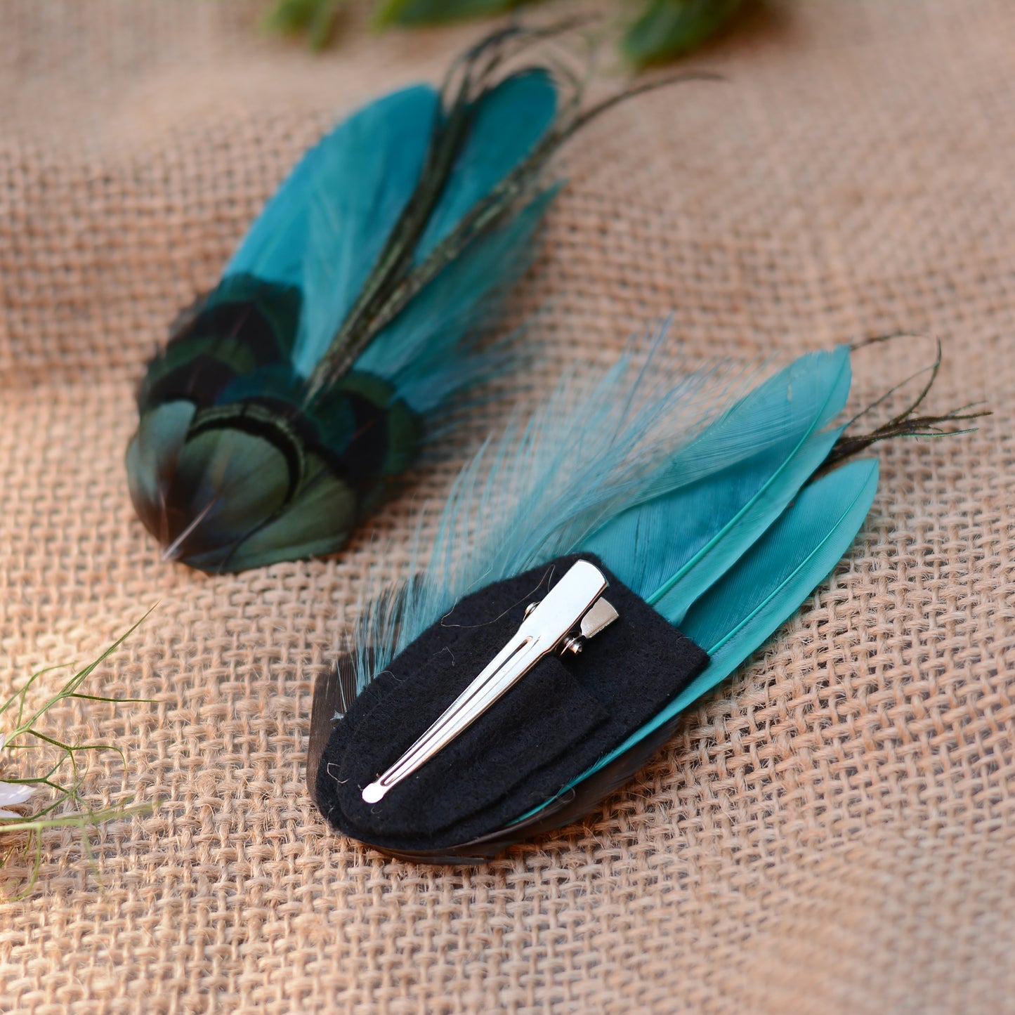 teal feather hair clip with iridescent green feathers on a burlap background with flowers
