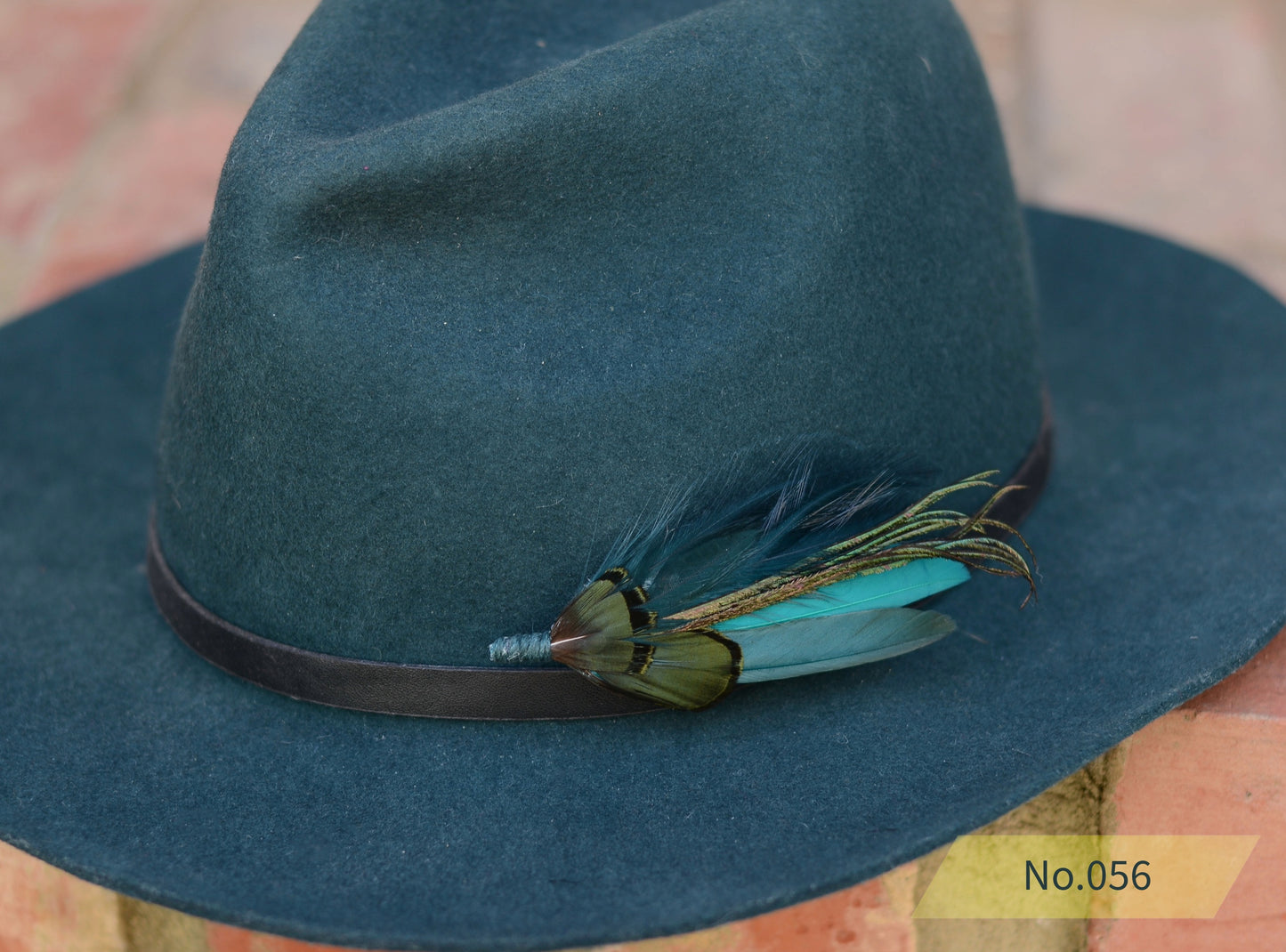Teal hat with feather hat pin detail on a blurred background