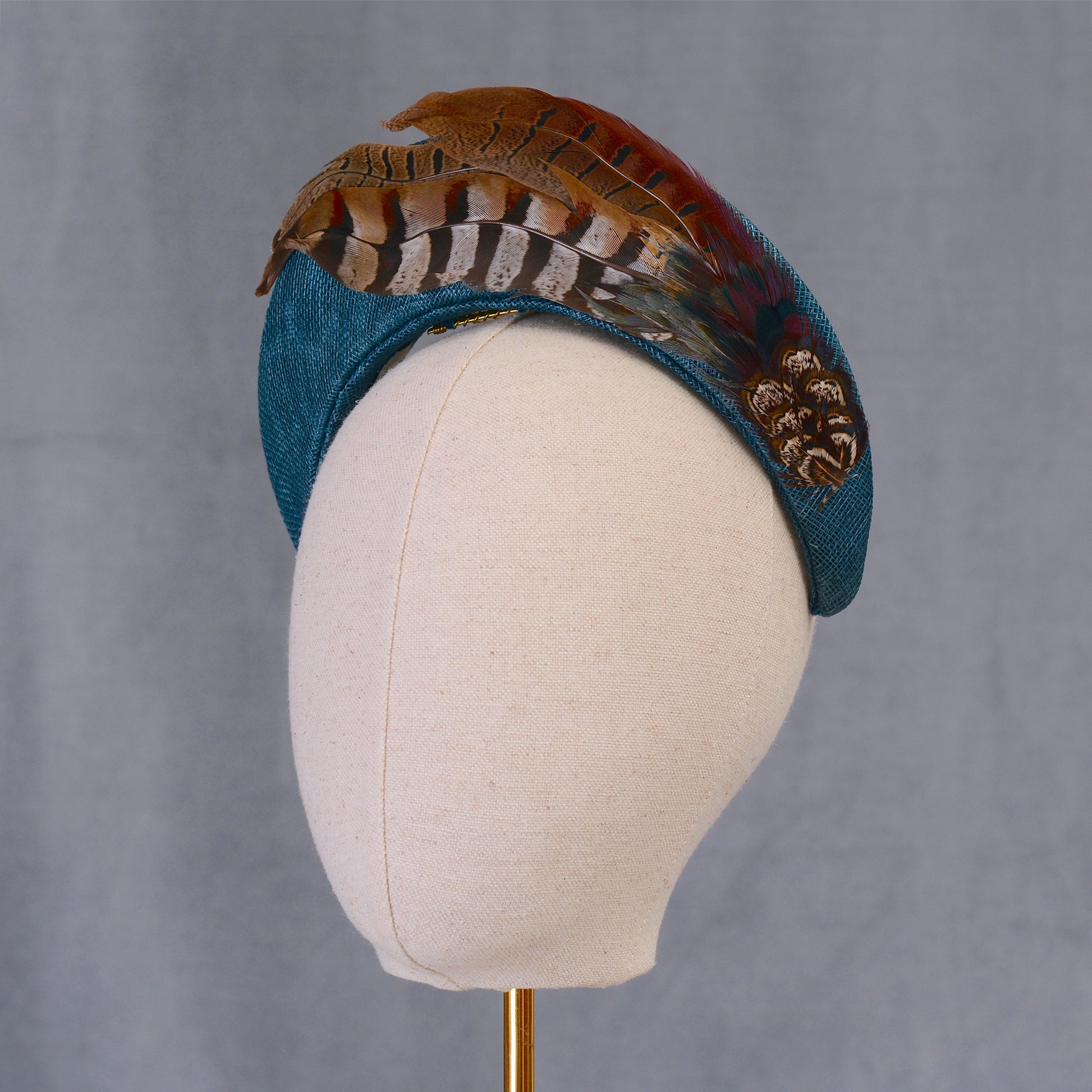 A teal turquoise bandeau style fascinator hand crafted in sinamay straw adorned with natural pheasant feathers with beautiful natural markings and earthy tones. Perfect for autumn weddings, horse racing and events.