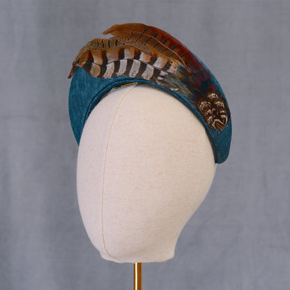 A teal turquoise bandeau style fascinator hand crafted in sinamay straw adorned with natural pheasant feathers with beautiful natural markings and earthy tones. Perfect for autumn weddings, horse racing and events.