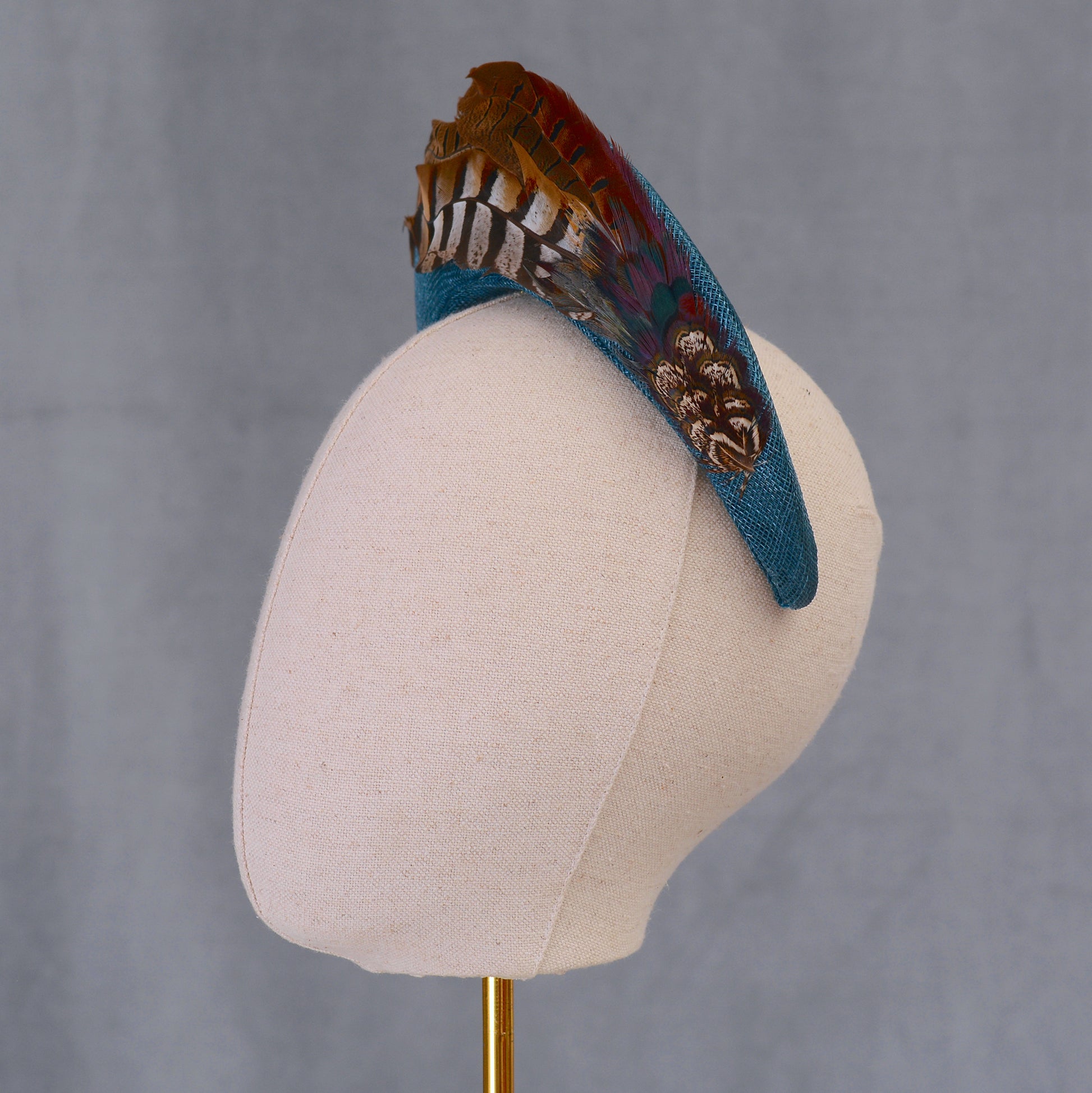 Decorative teal headband with pheasant feathers on a mannequin head against a gray background