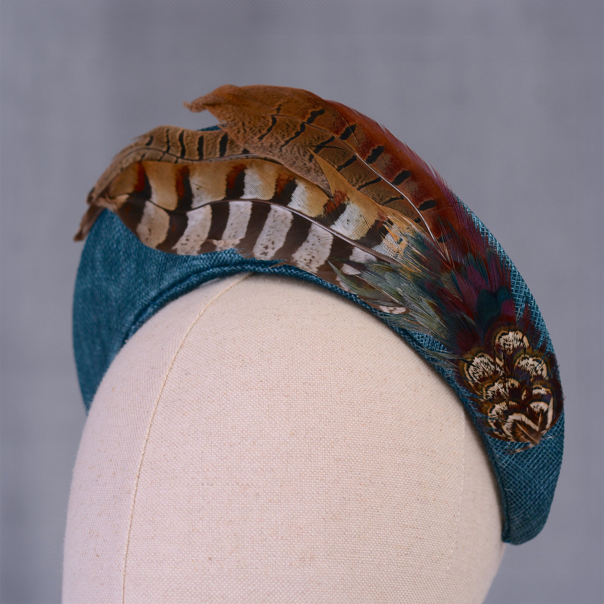 Teal Blue headband with feathers on a mannequin head against a gray background