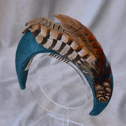 Teal blue occasion headband with feather accents on a grey  background
