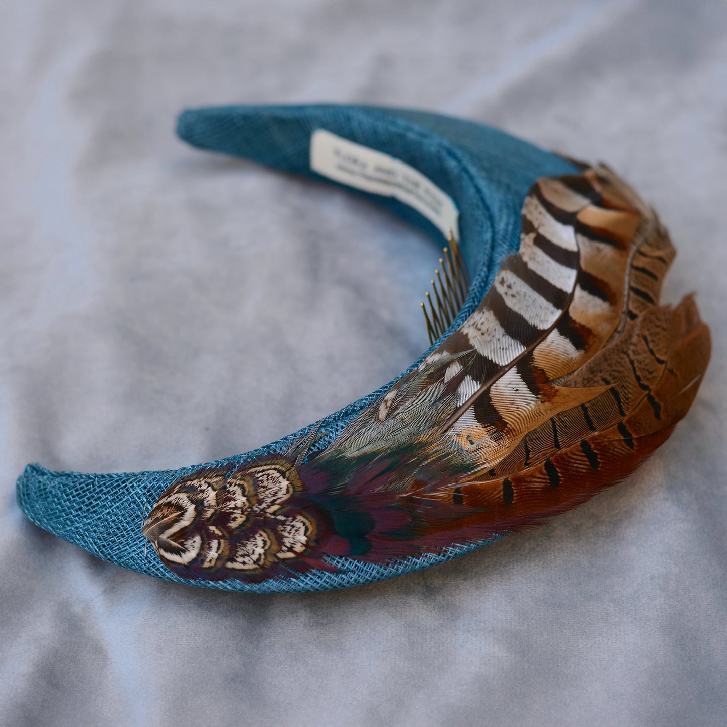 Teal blue occasion headband with feather accents on a grey  background