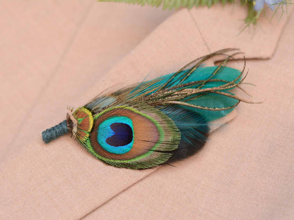 Close up of a  decorative peacock feather boutonniere pin accent, pinned to a beige suit jacket with a blue flower and green fern in background.