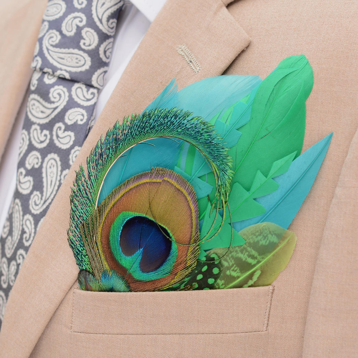 A close-up of a beige suit jacket with a white dress shirt, a grey paisley tie, and a vibrant green and turquoise  peacock feather pocket square in the breast pocket.