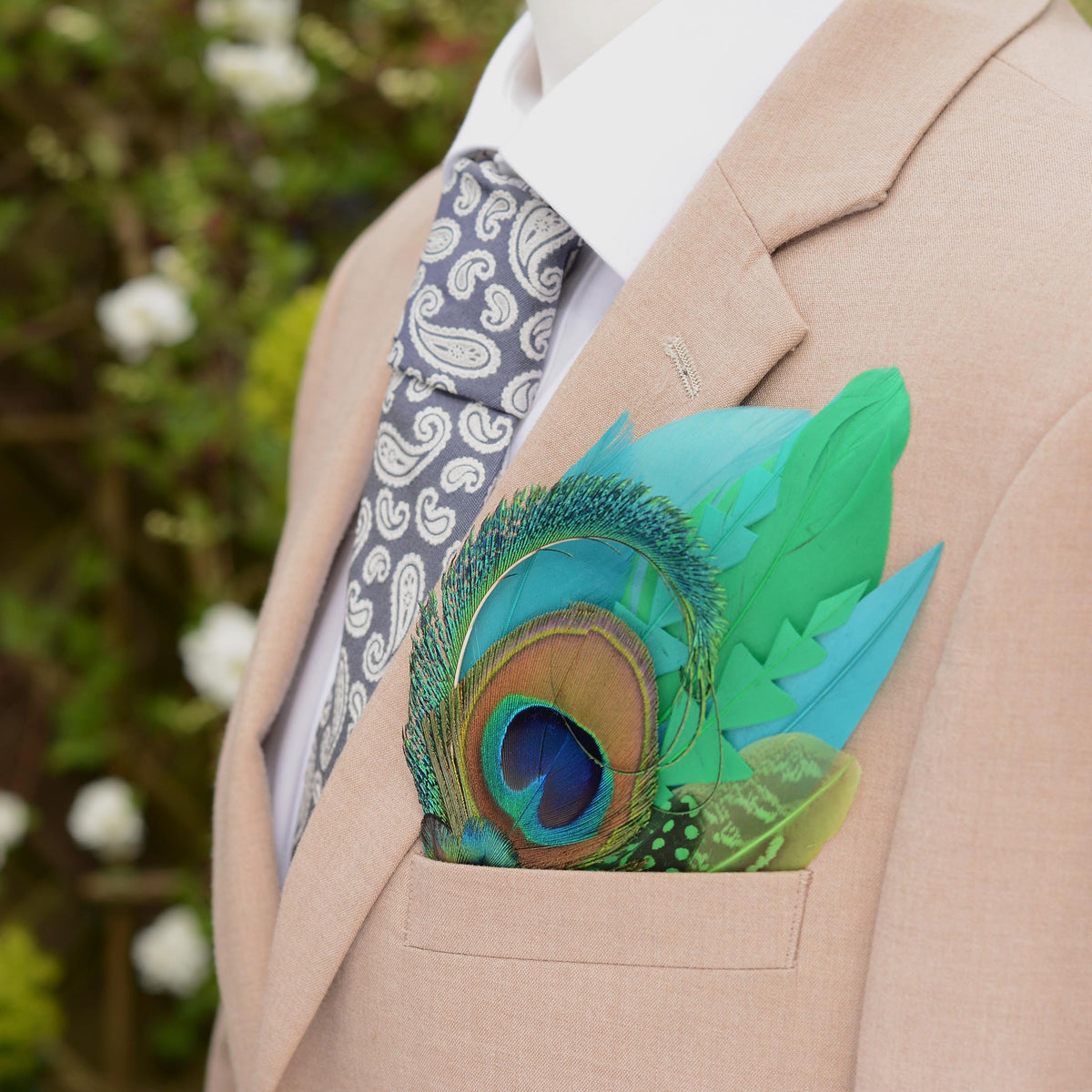 A close-up of a beige suit jacket with a white dress shirt, a grey paisley tie, and a vibrant green and turquoise  peacock feather pocket square in the breast pocket.